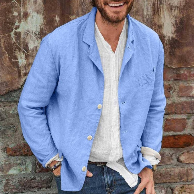 Man wearing a light blue jacket over a white shirt, standing against a brick wall.
