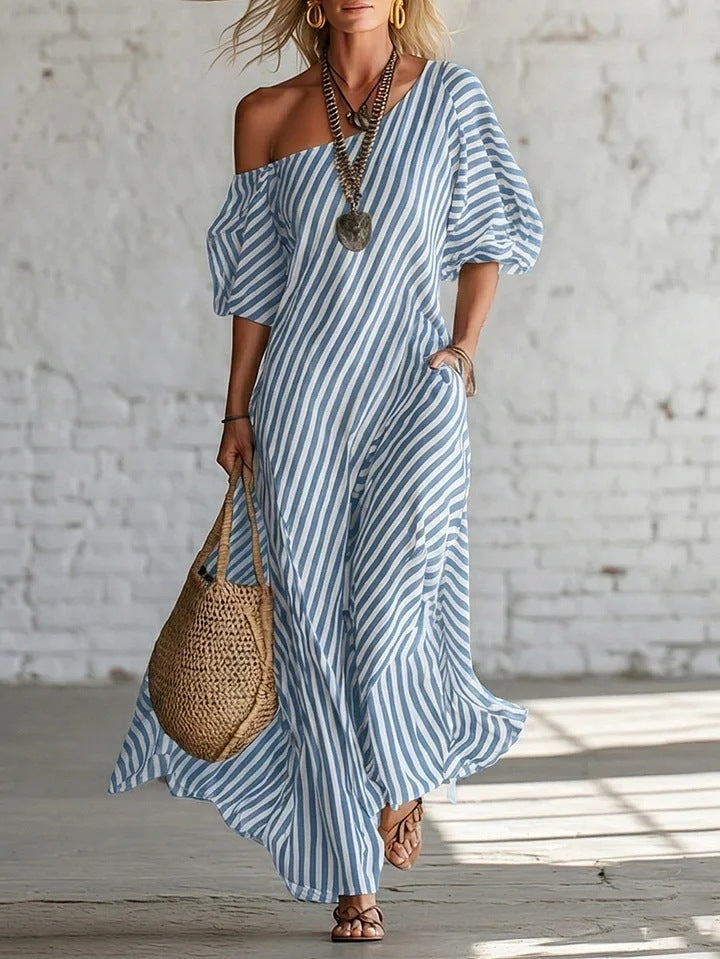 Woman wearing a blue and white striped dress holding a woven bag against a light-colored wall.