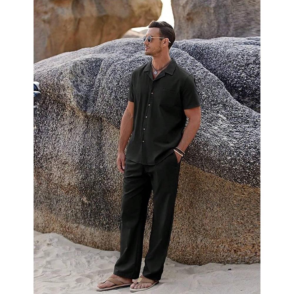 Man in black shirt and pants standing against large rocks on a beach