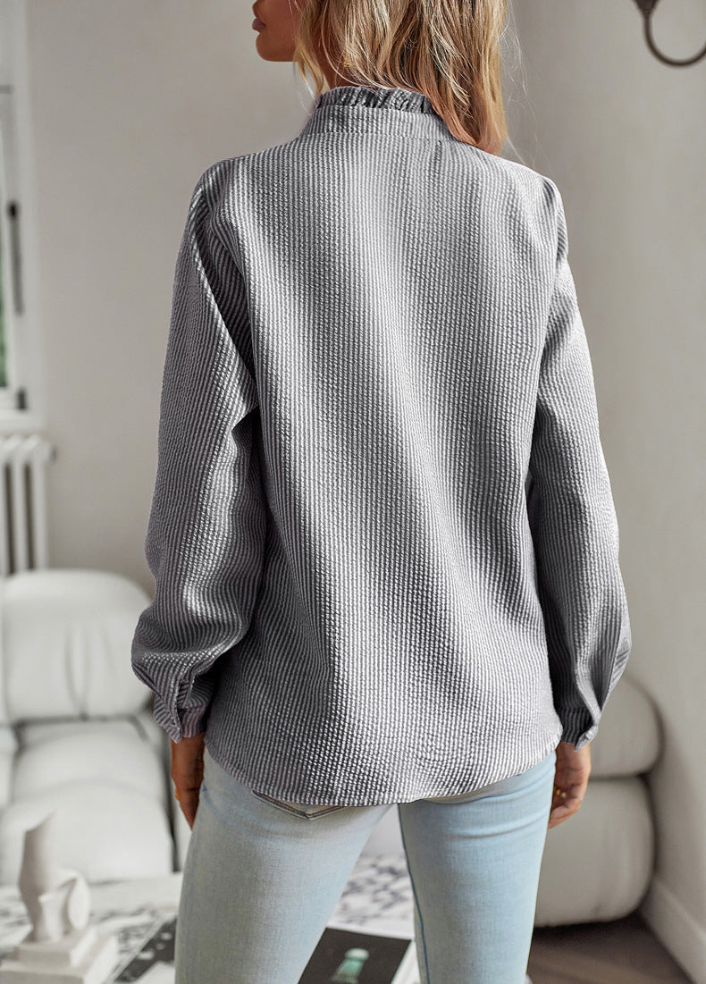 Person wearing a textured gray shirt and light blue jeans in a room with neutral decor.