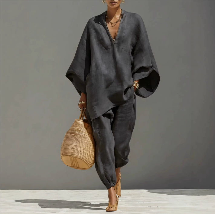Person wearing a dark gray outfit holding a woven bag against a plain background