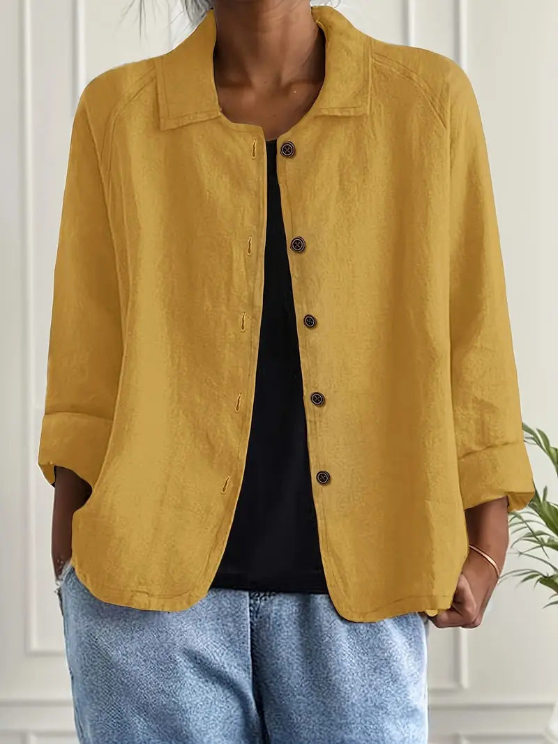 Person wearing a mustard yellow jacket over a black top and blue jeans indoors.