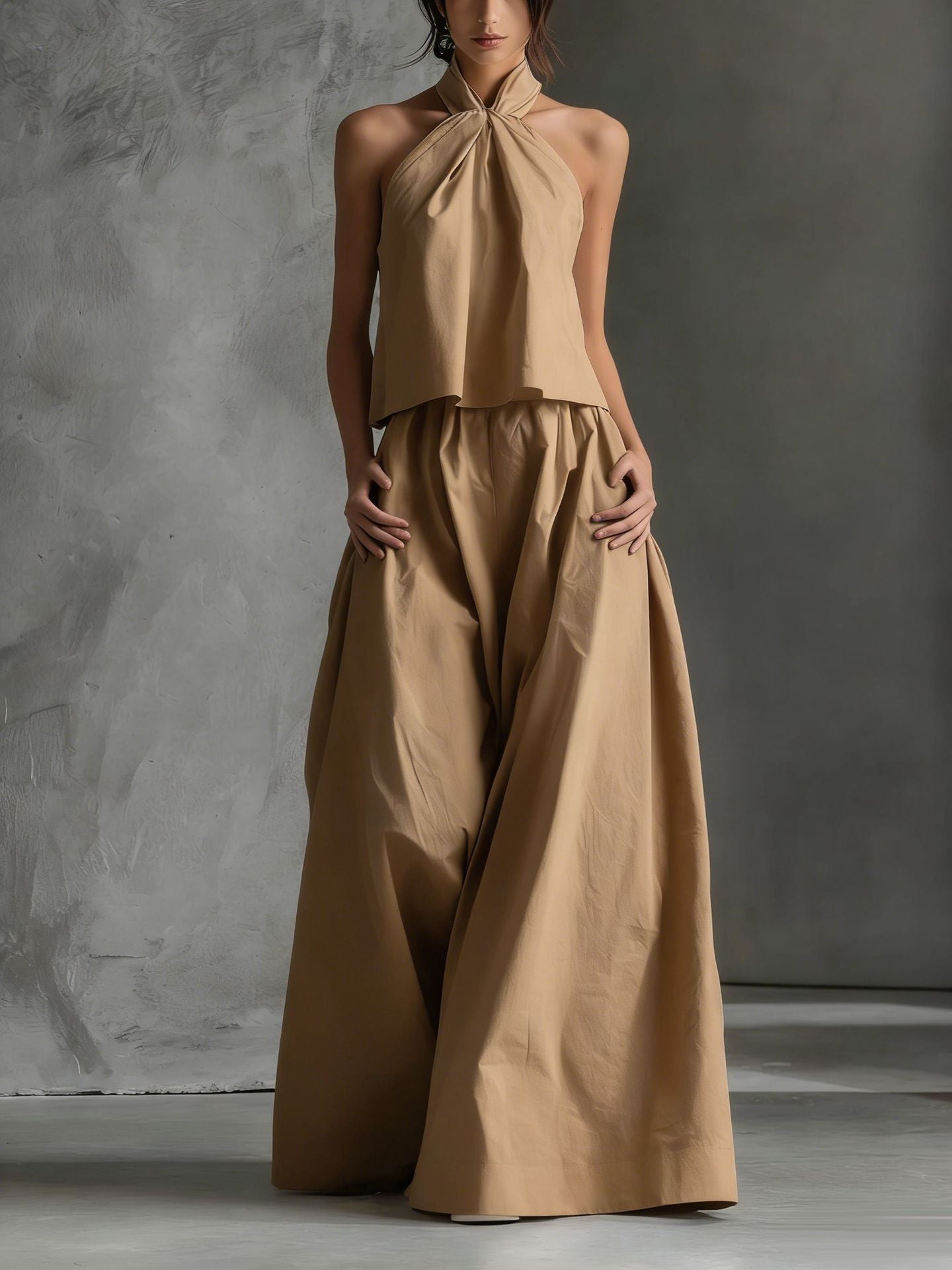 Woman wearing a beige halter top and wide-leg pants against a gray background