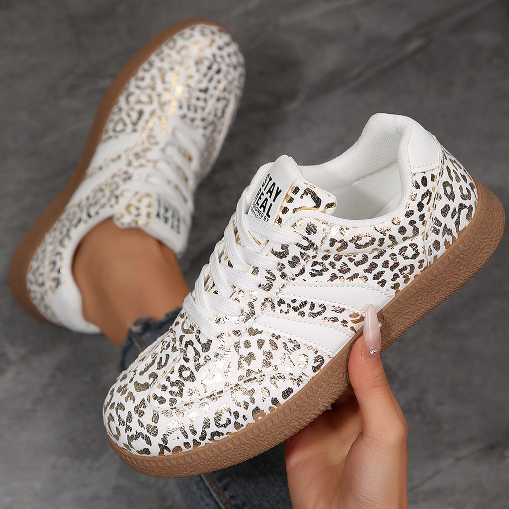 White sneakers with leopard print pattern and brown soles held by a hand on a gray background