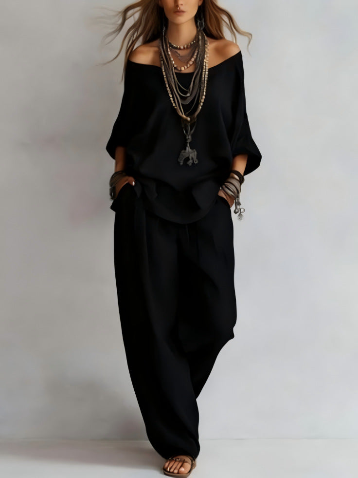 Person wearing a black outfit with layered necklaces on a plain background