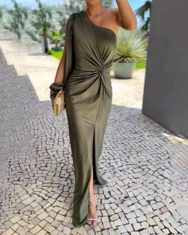 Woman in a green one-shoulder dress standing on a stone path with plants in the background