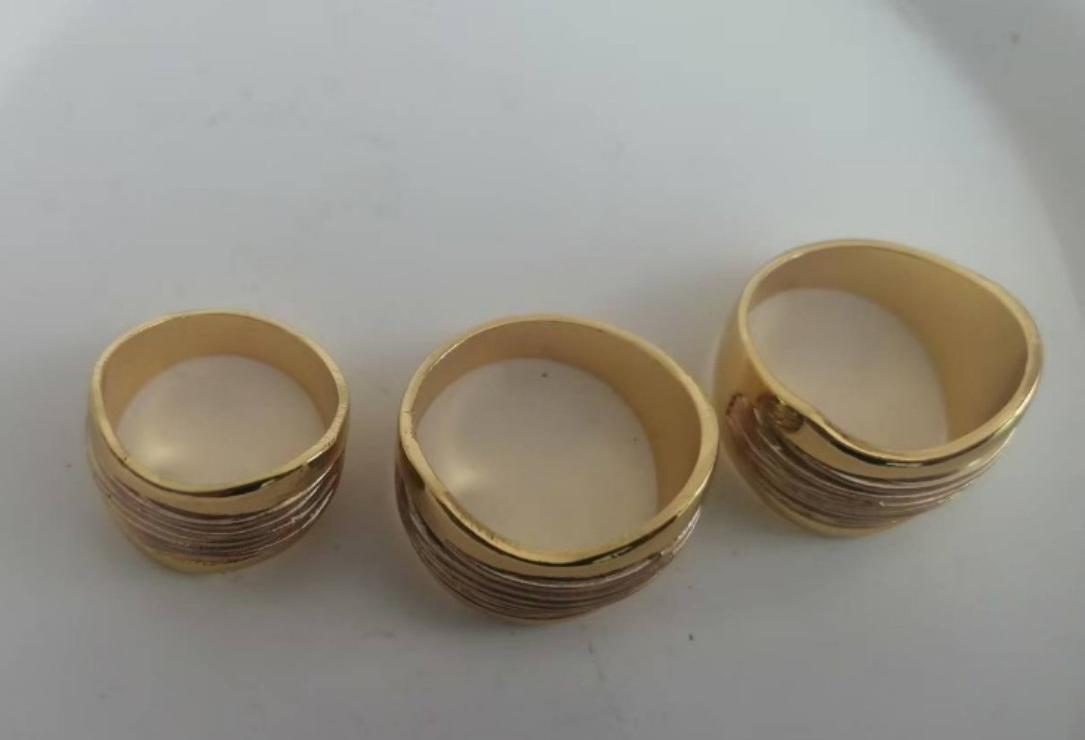 Three gold rings of different sizes on a white surface