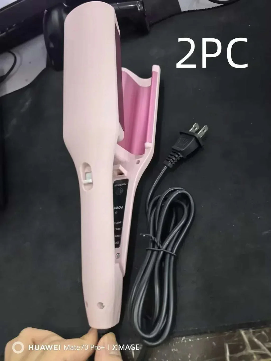 Pink electric hair curler with power cord on black surface, beauty hair styling tool