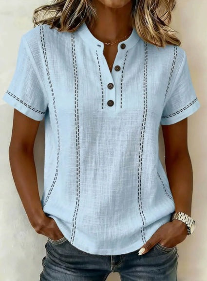Light blue short-sleeve shirt with button details worn by a person against a neutral background