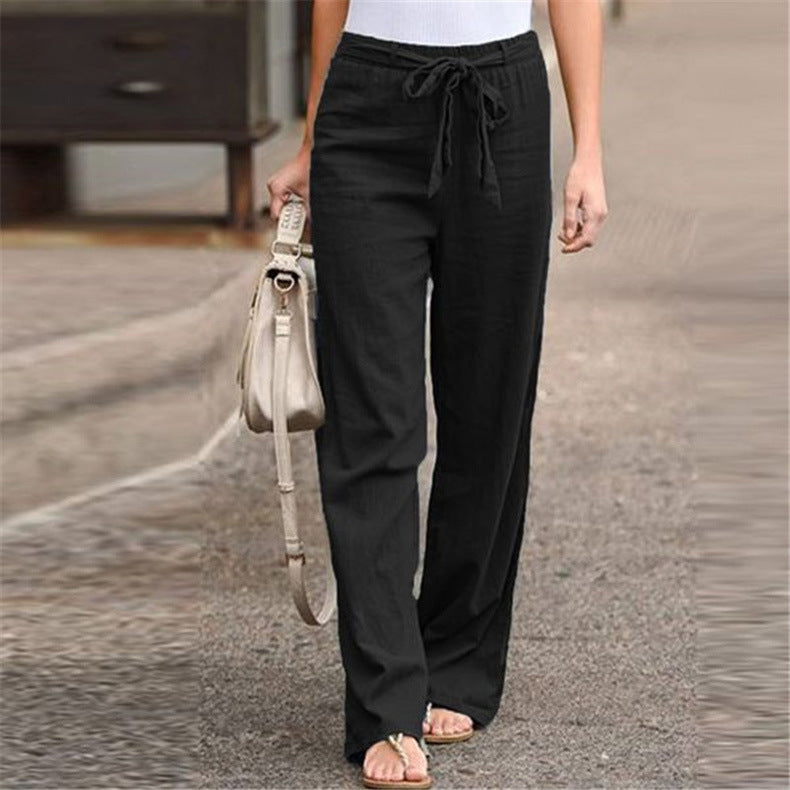 Person wearing black pants and sandals, holding a beige handbag on a street.