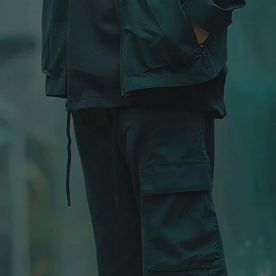 Person wearing a dark green jacket and pants in a blurred natural setting