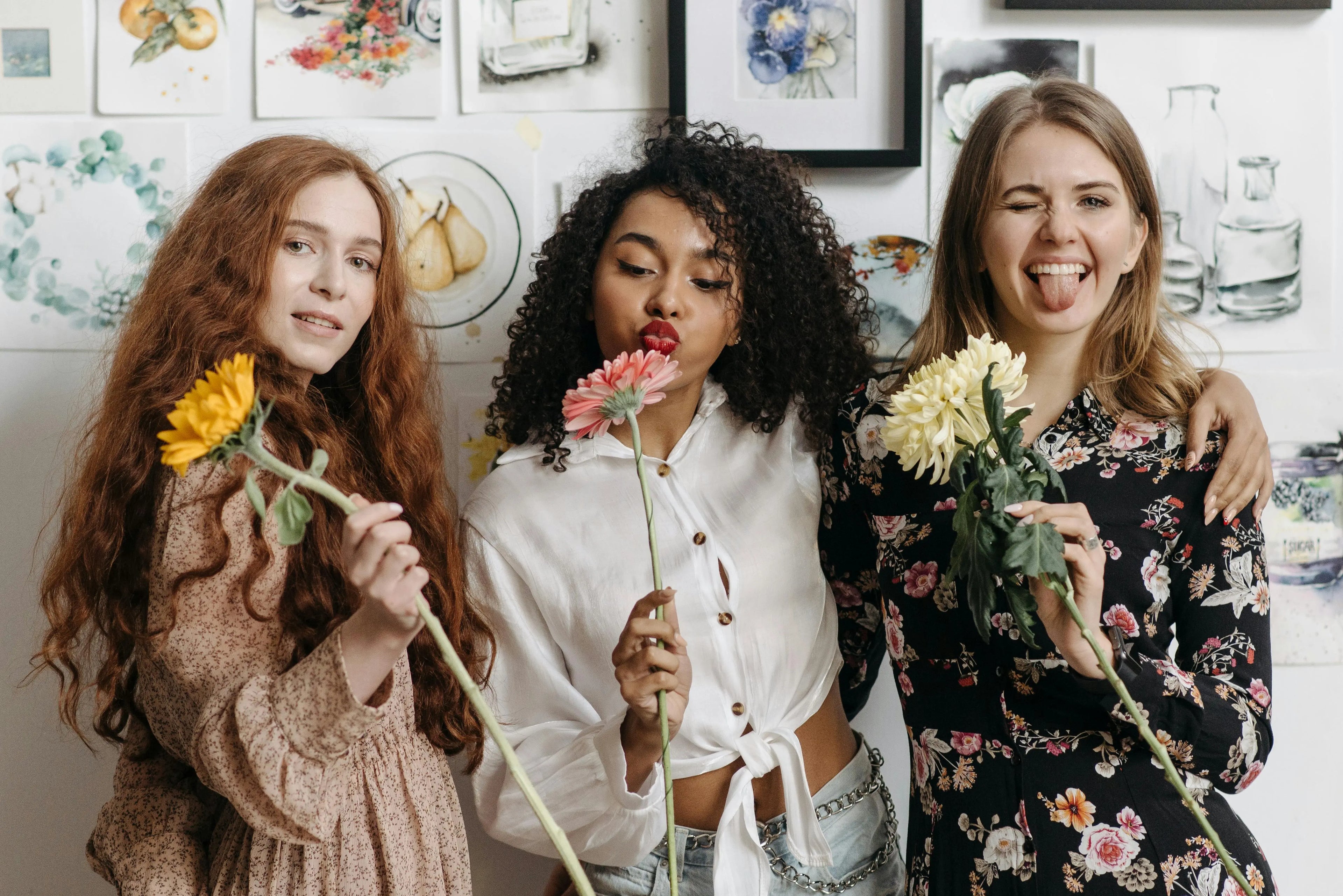 Three women holding flowers indoors with a decorative wall in the background